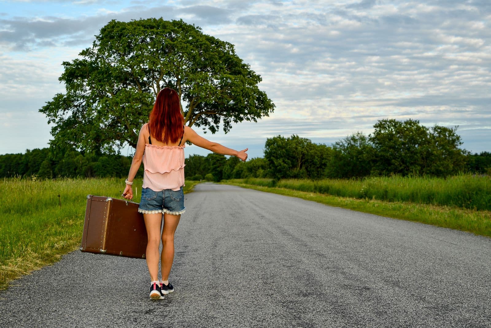 A traveler with a suitcase hitchhiking on a scenic open road
